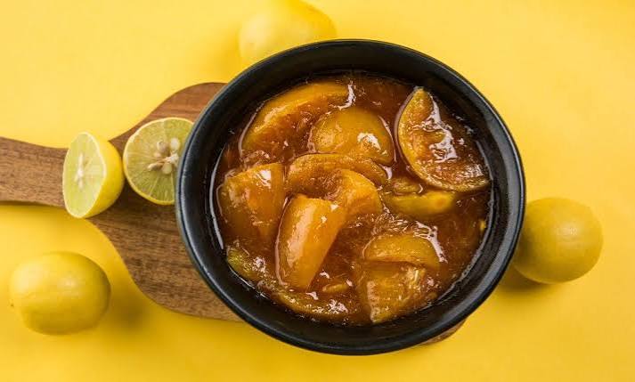 Homemade nimbu ka achaar (lemon pickle) in a bowl with fresh lemons
